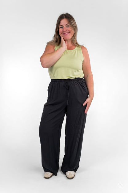 Smiling woman wearing sweetlegs Breeze Wide-Leg Pant in black paired with light green sleeveless top on white background