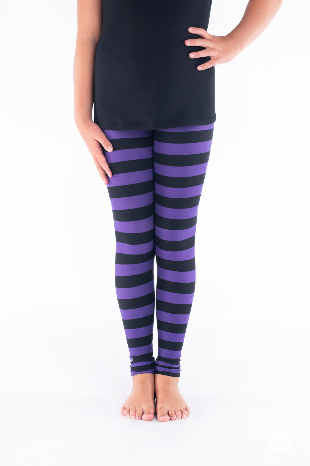Child wearing SweetLegs Toil and Trouble Kids leggings with black and purple horizontal stripes standing barefoot