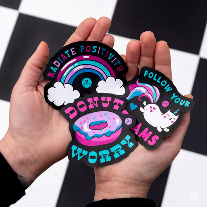 Hands holding SweetLegs Happiness Sticker Pack featuring colorful donut, rainbow, and unicorn designs with positive phrases